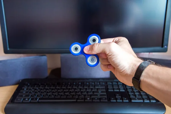 Mans mano sostiene un hilandero en el fondo de una computadora personal de cerca — Foto de Stock