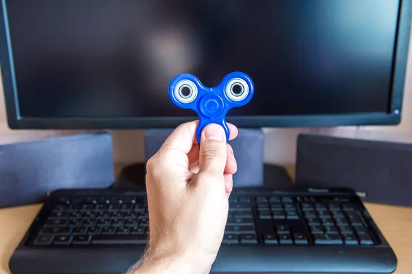 Mans mano sostiene un hilandero en el fondo de una computadora personal de cerca — Foto de Stock