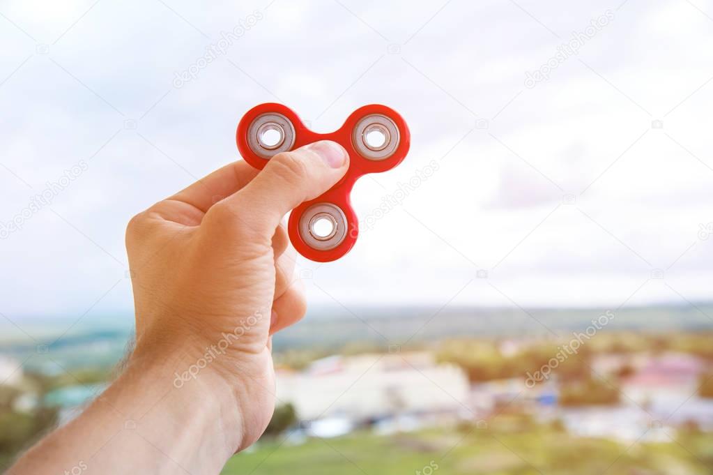 The hand plays with a spinner against the background of the urban landscape in the city fidgeting hand toy