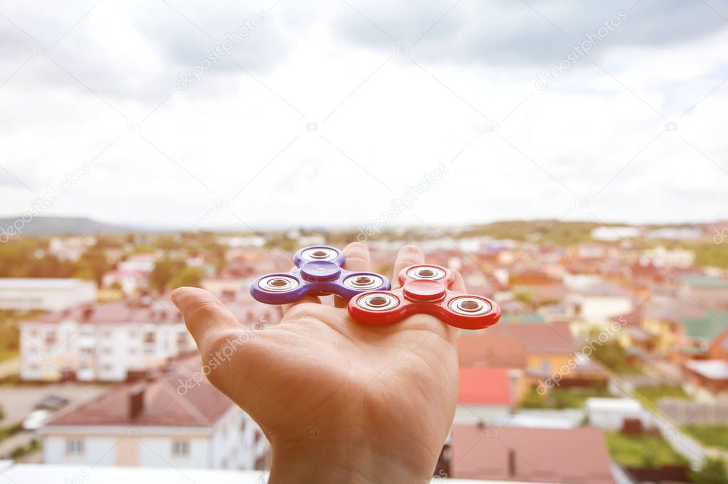Close-up of a hand of a man holding a two spinners machine on the background of a cityscape fidgeting hand toy