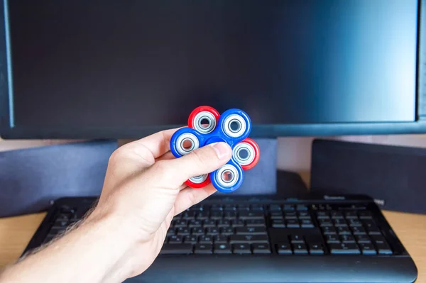 Mans mano sostiene dos hilanderos multicolores en el fondo de una computadora personal de cerca — Foto de Stock