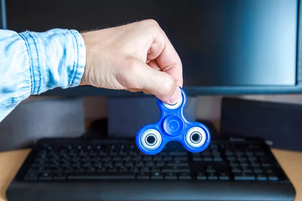 Mans mano sostiene un hilandero en el fondo de una computadora personal de cerca — Foto de Stock