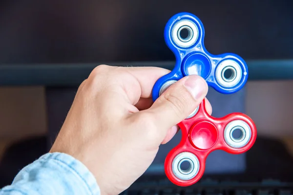 Mans hand holds two multi-colored spinners on the background of a personal computer close-up — Stock Photo, Image