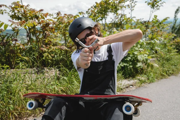Güneş gözlüğü ve tulum kafasını bir kask ile genç bir adam açık havada onun longboard üzerinde arabası değiştirir — Stok fotoğraf