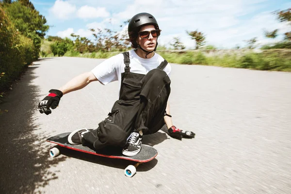 Joven con casco va a deslizarse, deslizarse con chispas en un longboard en el asfalto — Foto de Stock