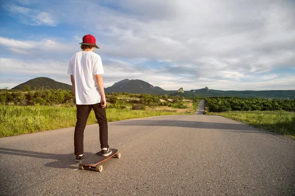 Ein junger Kerl - ein Skater mit Mütze wartet auf ein Rennen auf einer Landstraße — Stockfoto