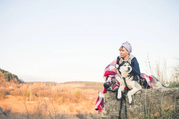 Genç bir kız arkadaşıyla beraber gorge kenarına husky köpek günbatımında oturur — Stok fotoğraf