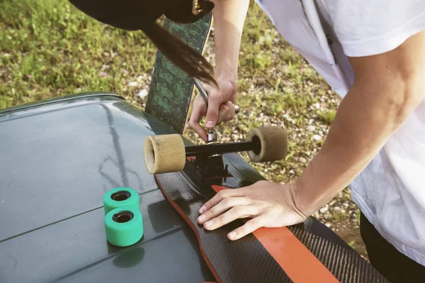 A close-up of a young guy changes his wheels on his longboard and adjusts the suspension. — Stock Photo, Image