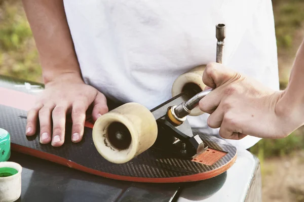Um close-up de um jovem muda suas rodas em seu longboard e ajusta a suspensão . — Fotografia de Stock