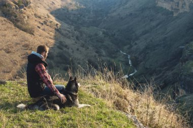 Doğada köpeğini yürüyüşe bir sakallı bir adam, sıcak bir döküm yükselen güneş, bir arka ışık ile ayakta kızdırma ve uzun gölgeler gorge ve ağaçlar arka planı.