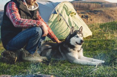 Çadır yanındaki doğa günbatımı de akşam oturup tatil kot kareli gömlek ve kolsuz ceket köpek kabuğu ile yakın çekim adam sakallı