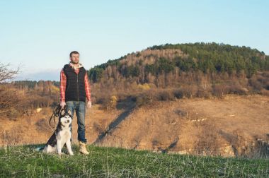 Doğada köpeğini yürüyüşe bir sakallı bir adam, sıcak bir döküm yükselen güneş, bir arka ışık ile ayakta kızdırma ve uzun gölgeler gorge ve ağaçlar arka planı.