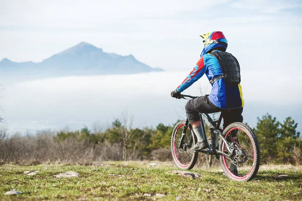 Un giovane ragazzo in piedi sulla tua mountain bike in cima a una montagna, quando sotto le montagne basse nuvole — Foto Stock