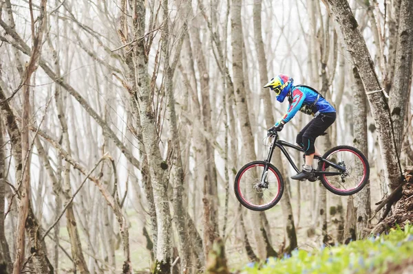 Un ciclista in mountain bike salta da un trampolino di lancio in una foresta nebbiosa, nelle montagne del Caucaso — Foto Stock