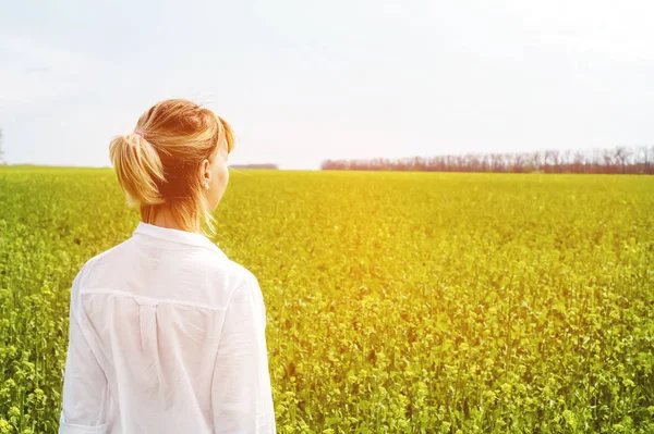 The beauty of a girl outdoors, enjoying nature and freedom and enjoying life. Beautiful girl in a white shirt, strolls on a spring field, the sun warm light.