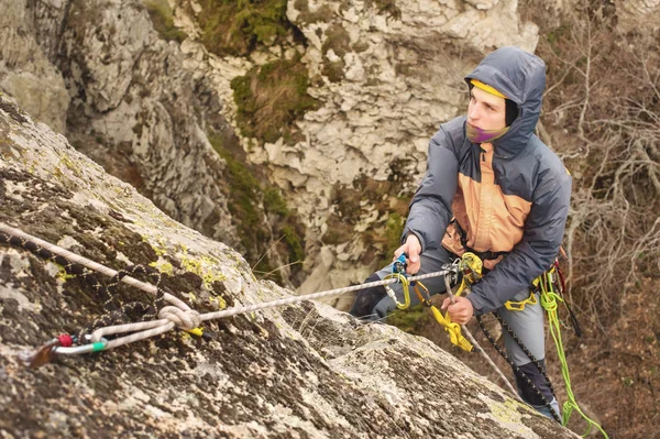 Młody człowiek rock wspina się na liny, pasy bezpieczeństwa, ubezpieczenia i liny, Sprzęt alpinistyczny pełny i kask — Zdjęcie stockowe