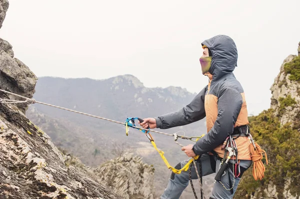 Mladý muž leze Skála na lano s bezpečnostními pásy, pojištění a lana, v plné Horolezecká výzbroj a helmu — Stock fotografie