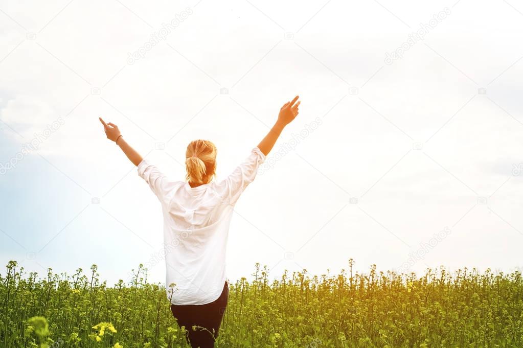 The beauty of a girl outdoors, enjoying nature and freedom and enjoying life. Beautiful girl in a white shirt, strolls on a spring field, the sun warm light.