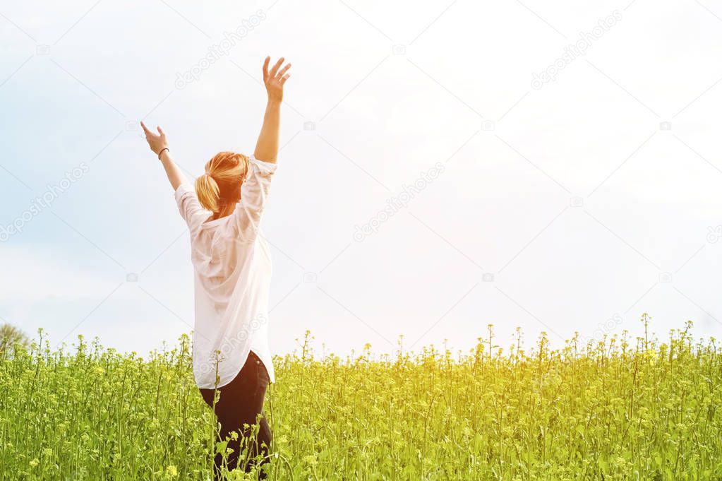 The beauty of a girl outdoors, enjoying nature and freedom and enjoying life. Beautiful girl in a white shirt, strolls on a spring field, the sun warm light.