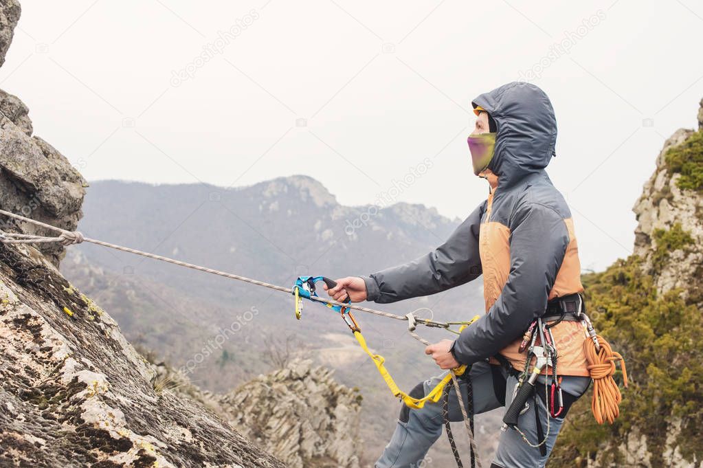 The Young Man climbs the rock on a rope with safety belts, insurance and rope, in full mountaineering equipment and a helmet