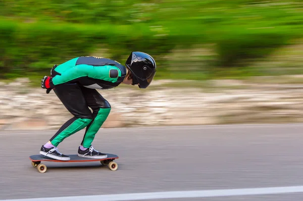 Kask içinde genç bir adam ve bir özel raf deri elbiseli bir longboard afsaltu arka plan dağlar ve güzel gökyüzü üzerinde sürmek — Stok fotoğraf