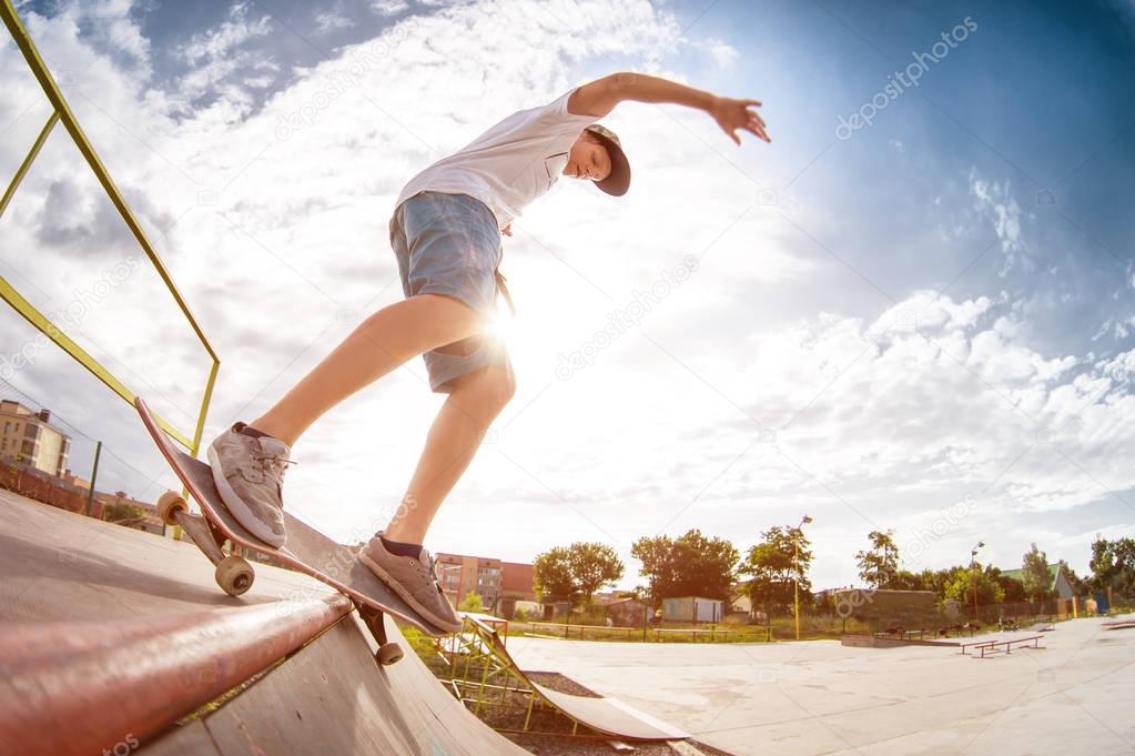 Teenager skater in a cap and shorts on rails on a skateboard in a skate park