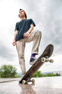 Bir kaykay üzerinde şehir manzara arka plan ile genç bir patenci duruyor