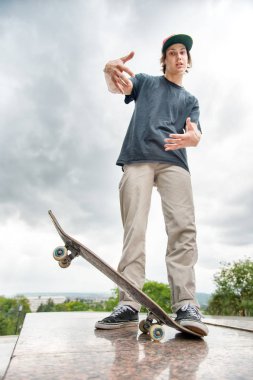 Bir kaykay üzerinde şehir manzara arka plan ile genç bir patenci duruyor