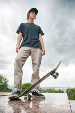 Bir kaykay üzerinde şehir manzara arka plan ile genç bir patenci duruyor
