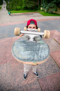 Bir kaykay üzerinde şehir manzara arka plan ile genç bir patenci duruyor