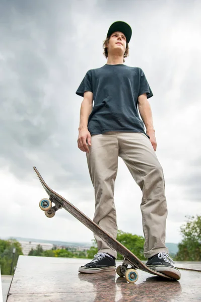 Bir kaykay üzerinde şehir manzara arka plan ile genç bir patenci duruyor