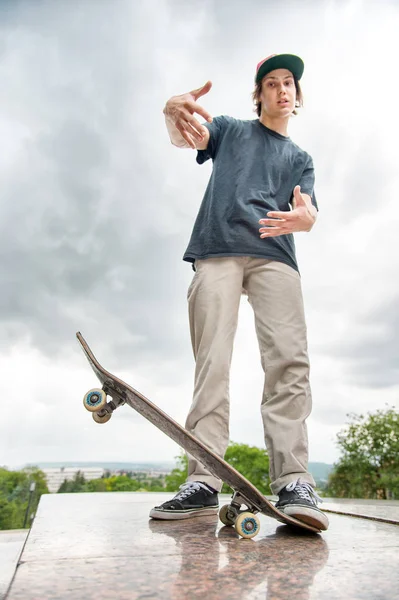 Bir kaykay üzerinde şehir manzara arka plan ile genç bir patenci duruyor