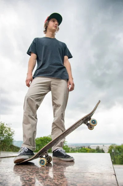 Bir kaykay üzerinde şehir manzara arka plan ile genç bir patenci duruyor