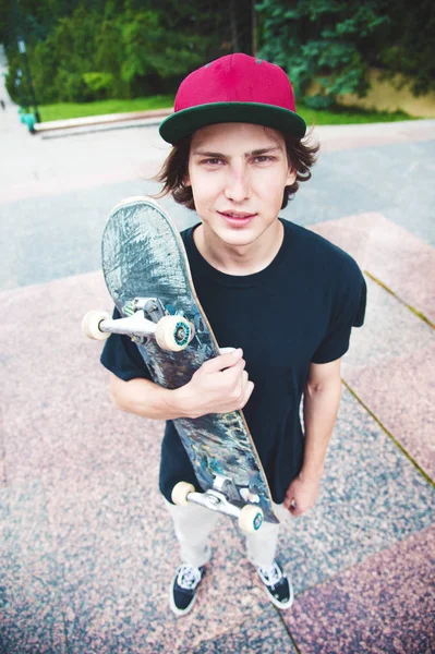 Ein junger Skater steht mit einem Skateboard vor dem Hintergrund der Landschaft der Stadt — Stockfoto