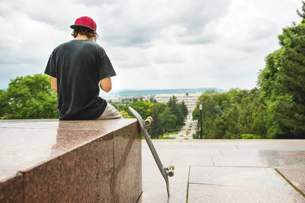 Skater siedzi tyłem i myśli, że obok deskorolka — Zdjęcie stockowe