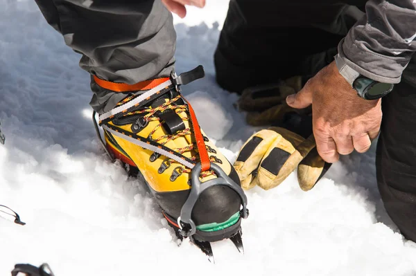 Een jonge kerel wandelaar jurken stijgijzers klimmen over bergbeklimmen schoenen voor het doorlopen van de gletsjer — Stockfoto