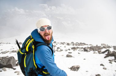 Şapka ve güneş gözlüğü takan bir sakallı rehber portresi dilini gösterir