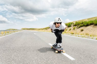 Kask ve güneş gözlüğü takan bir adam onun longboard bir ülke yolda biniyor