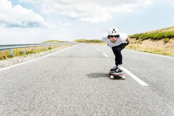 Kask ve güneş gözlüğü takan bir adam onun longboard bir ülke yolda biniyor