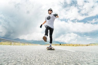 Bir adam bir kask ve güneş gözlüğü ayağını onun longboard üzerinde iterek hızlandırır