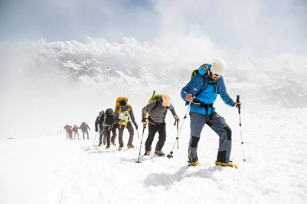 En grupp bergsklättrare klättrar till toppen av ett snöklädda berg — Stockfoto