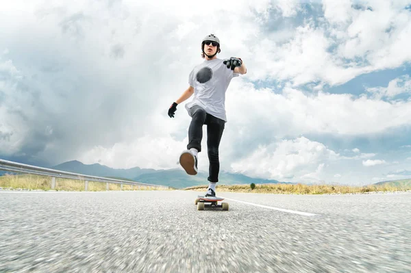 Een man in een helm en zonnebril versnelt zijn voet te duwen op zijn longboard — Stockfoto