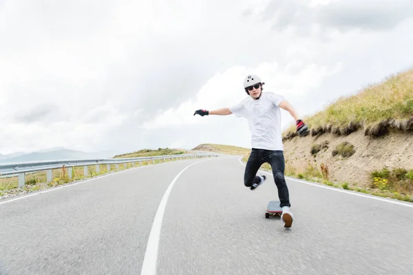 Um jovem hipster em um capacete e luvas realizando um slide de pé em uma alta velocidade cai do tabuleiro — Fotografia de Stock