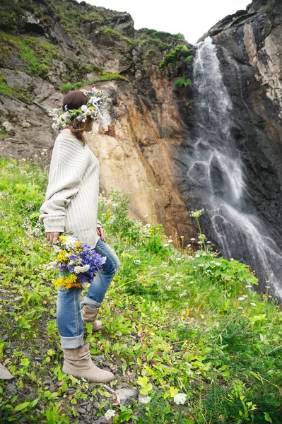 Ritratto di una ragazza con una ghirlanda in testa e un mazzo di fiori tra le mani contro una cascata — Foto Stock