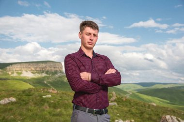 Genç bir adam elleriyle göğsünü karşı güzel bir manzara zemin üzerinde duruyor