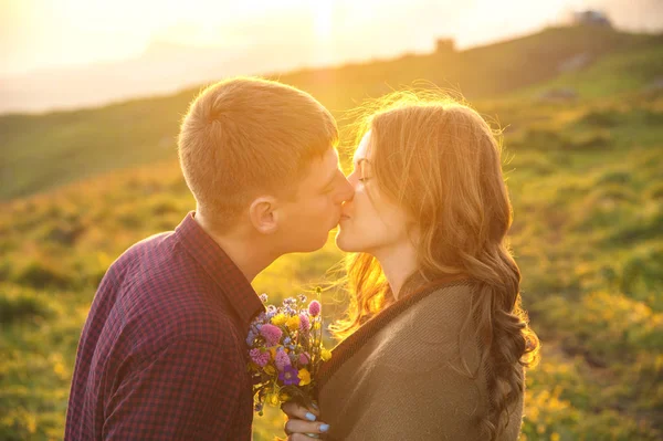 Joven pareja feliz besándose en la naturaleza contra el sol poniente al atardecer . — Foto de Stock