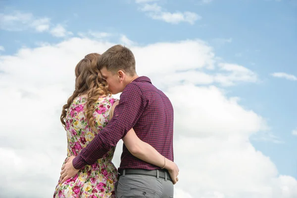 Вид со спины. Молодая пара обнимает поцелуи на фоне голубого неба и белых облаков . — стоковое фото