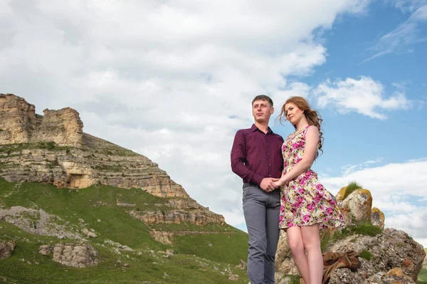 Pareja Joven con una chica cogida de la mano de pie y mirando hacia otro lado en el fondo de un hermoso paisaje de rocas y nubes — Foto de Stock