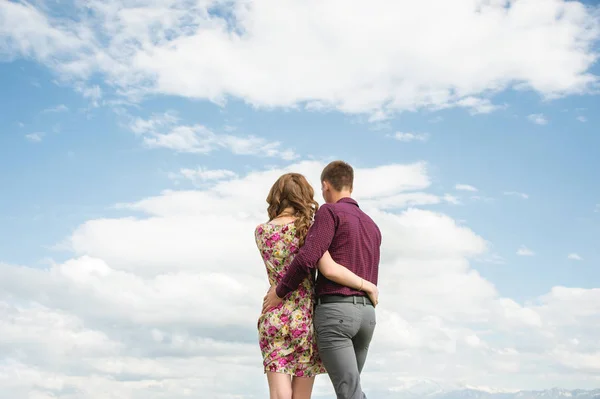 Вид с задней стороны молодой пары стоит в объятиях и смотрит вдаль на небо с облаками . — стоковое фото