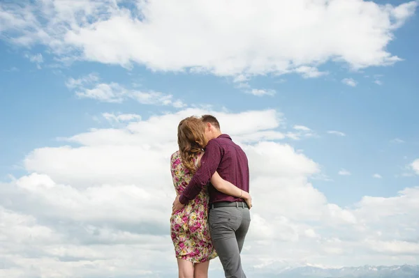 Вид ззаду. Молода пара обіймає поцілунки на блакитне небо і білі хмари . — стокове фото